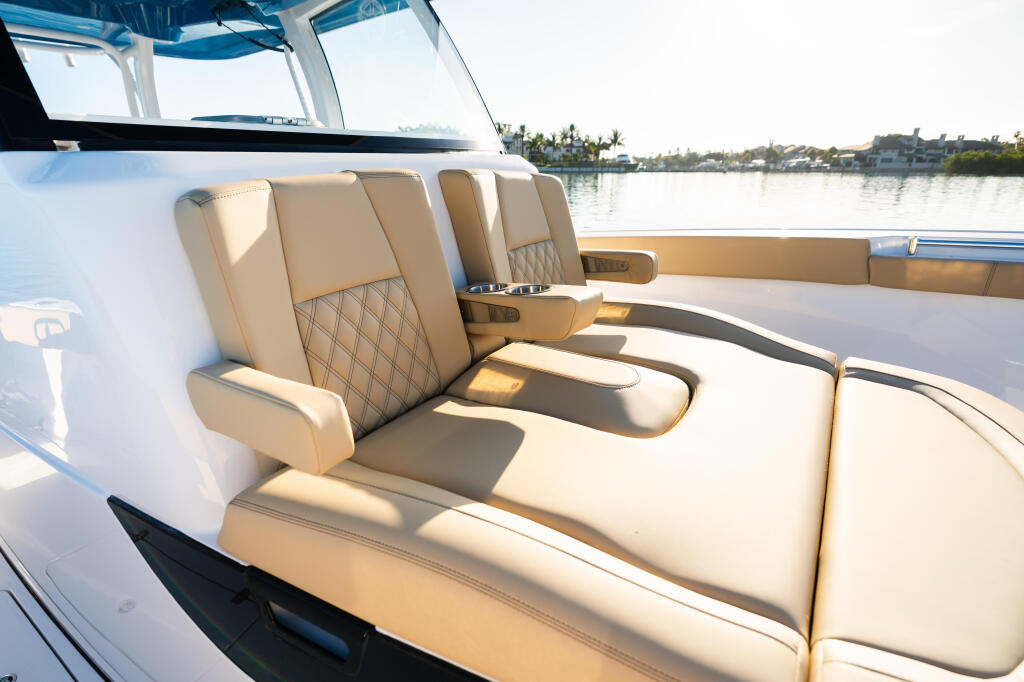 Cream-colored quilted seating and sun lounges on boat deck with waterfront homes visible in background