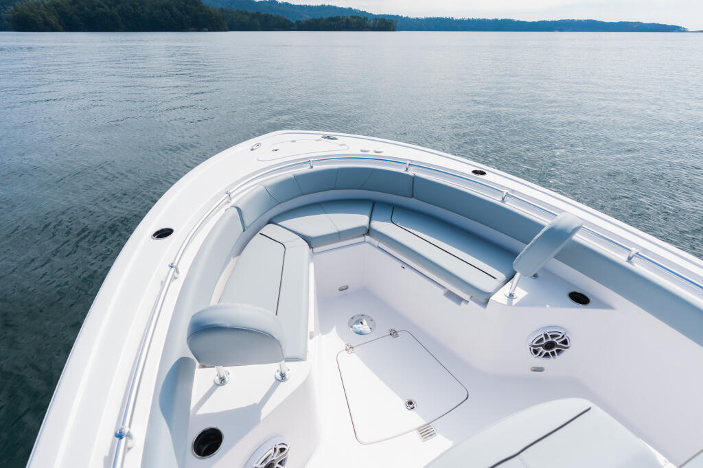 Spacious bow seating and console area of a white center console boat on calm lake water with forested shoreline