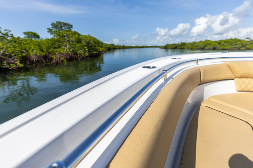 Boat's tan cushioned seating and white railings overlooking mangrove shoreline and calm blue water