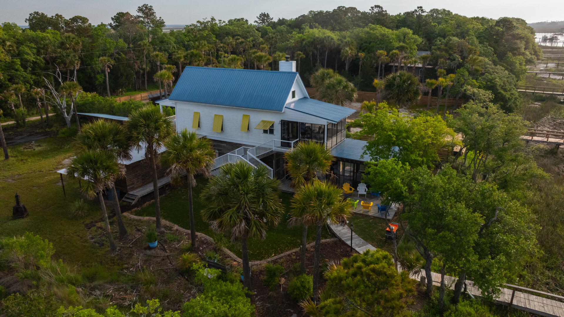 Aerial view of a modern waterfront home with blue metal roof surrounded by palm trees and wetlands