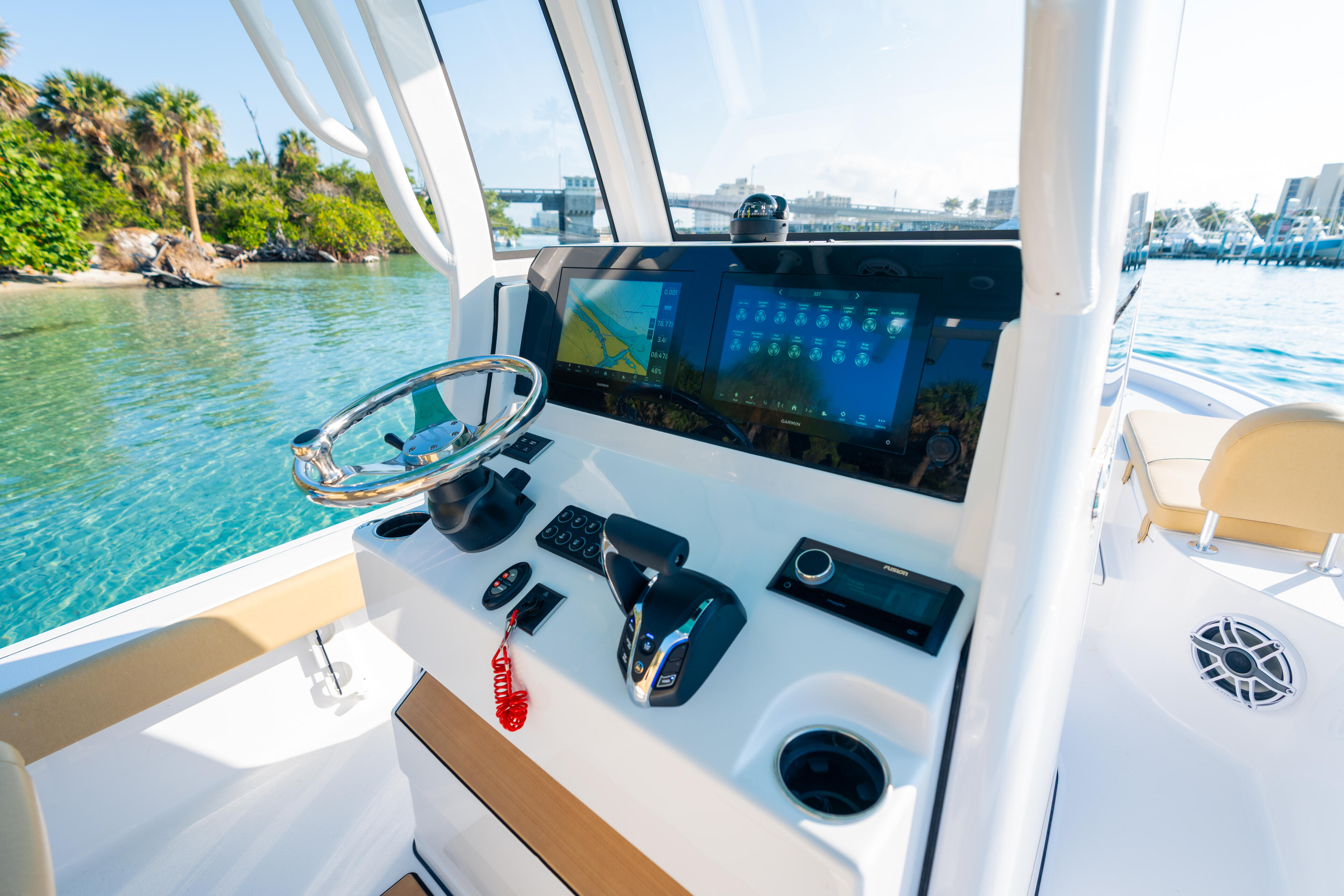 Helm station with large touchscreen display, steering wheel, and control panels overlooking tropical water and marina