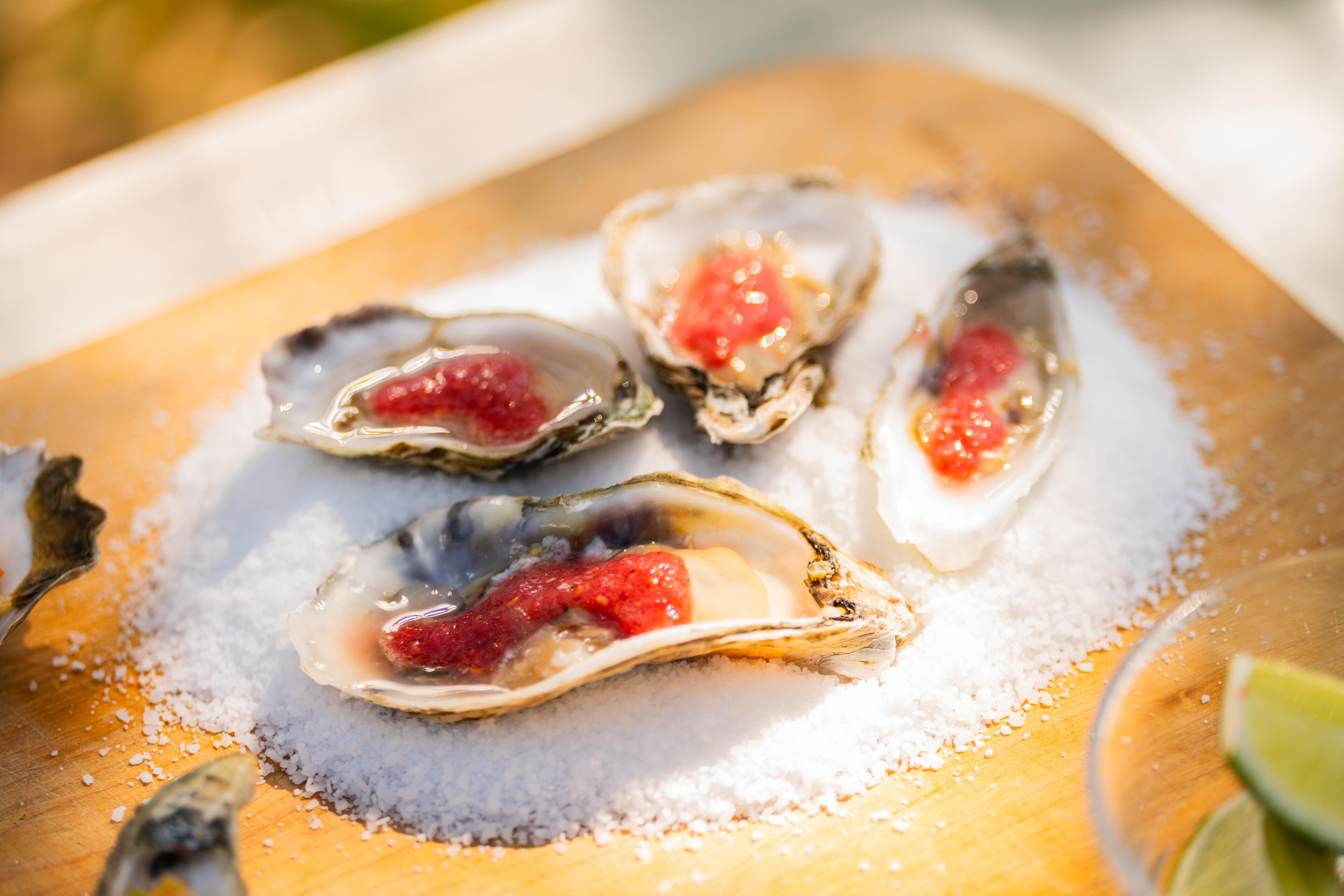 Fresh oysters topped with red roe served on ice on a wooden board