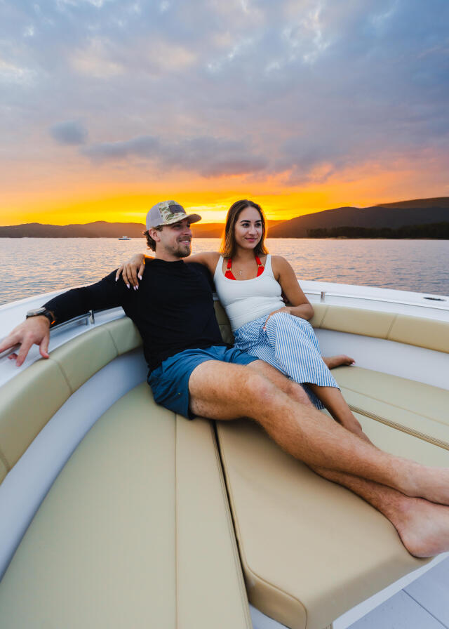 Couple relaxing on boat seating at sunset over the water with mountains in background