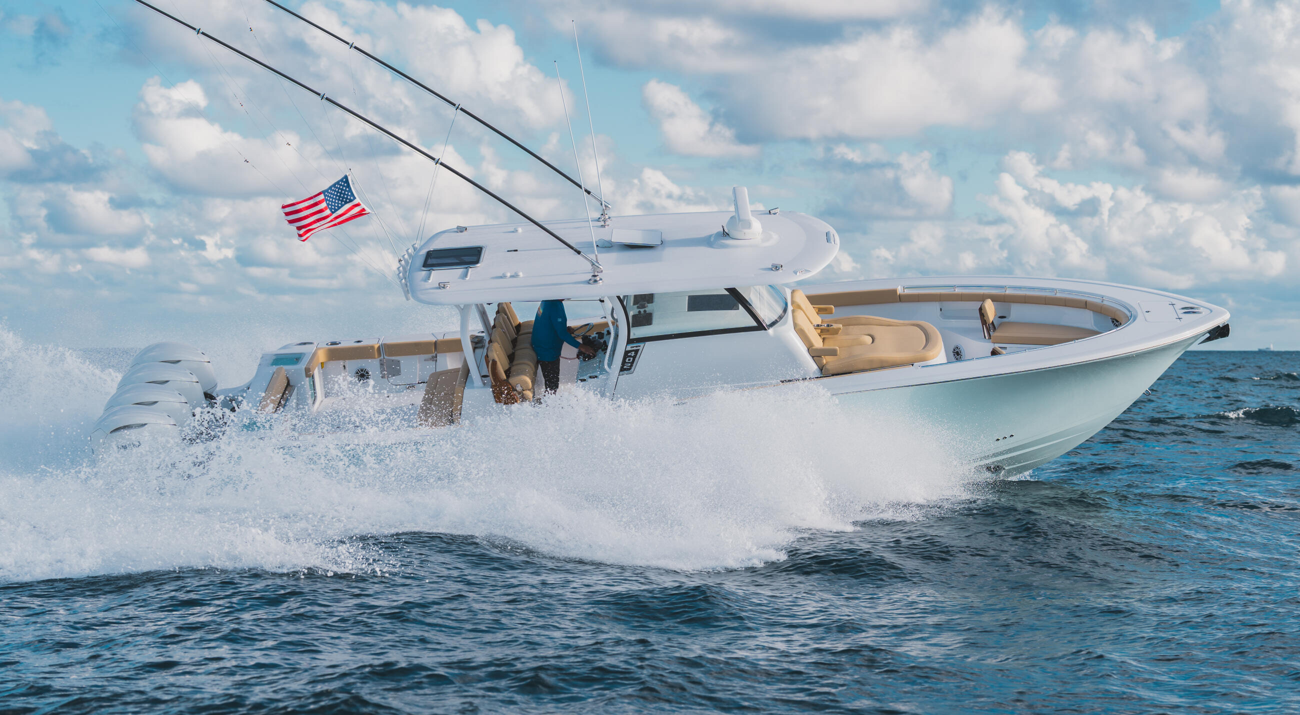 White sport fishing boat with tan interior running through waves offshore with American flag