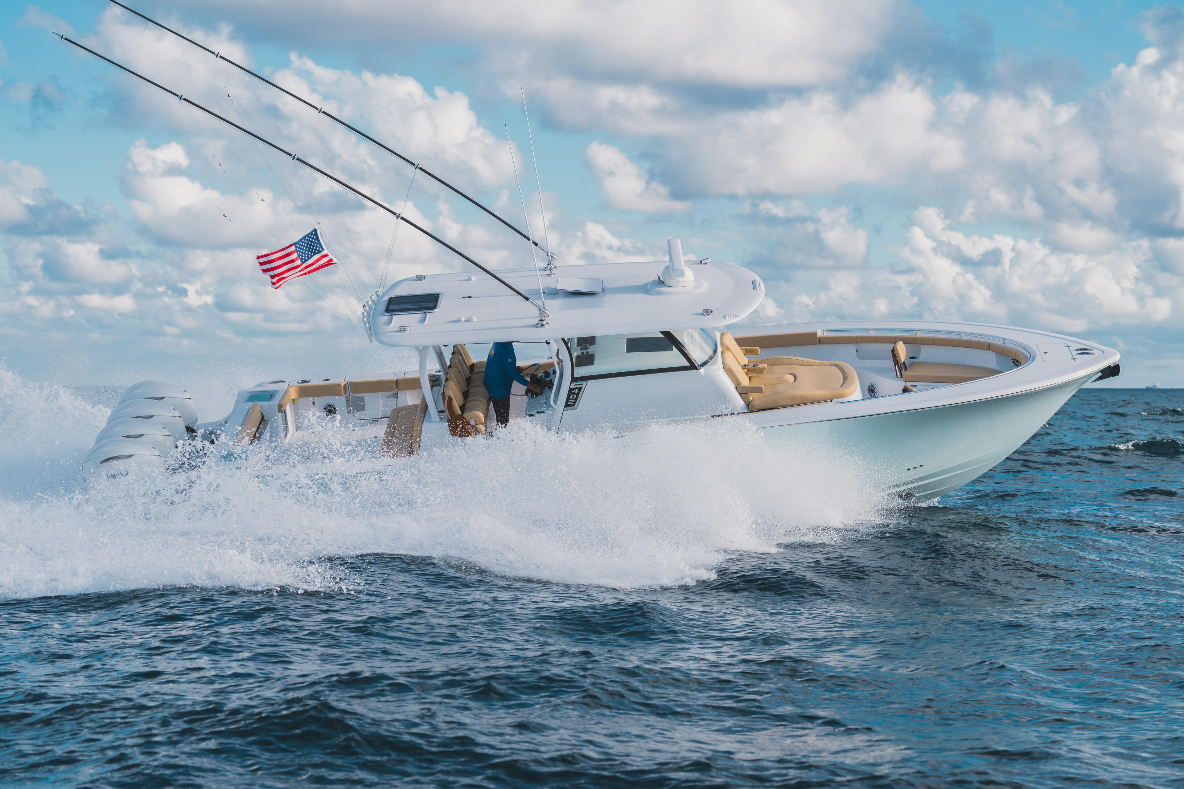 White sport fishing boat with tan interior running through waves offshore with American flag