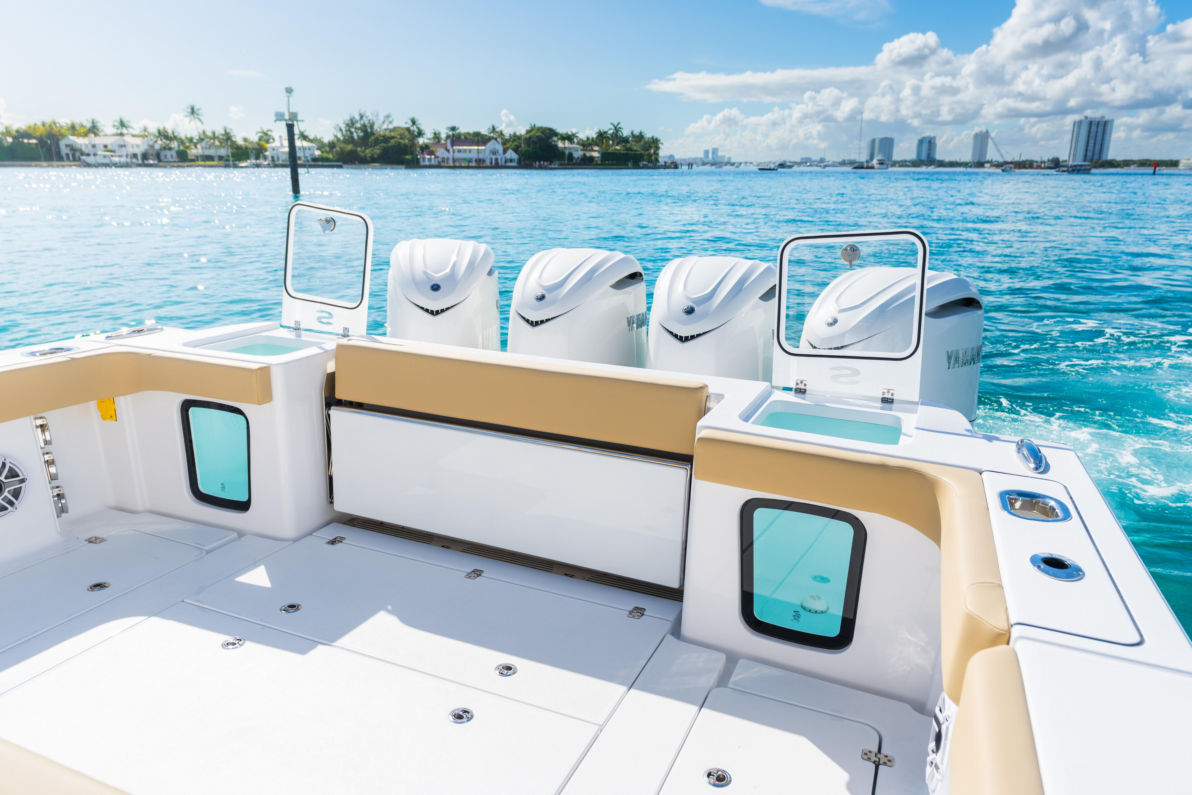 Center console boat with dual outboard engines and open cockpit with livewell storage visible against blue water and coastal city skyline