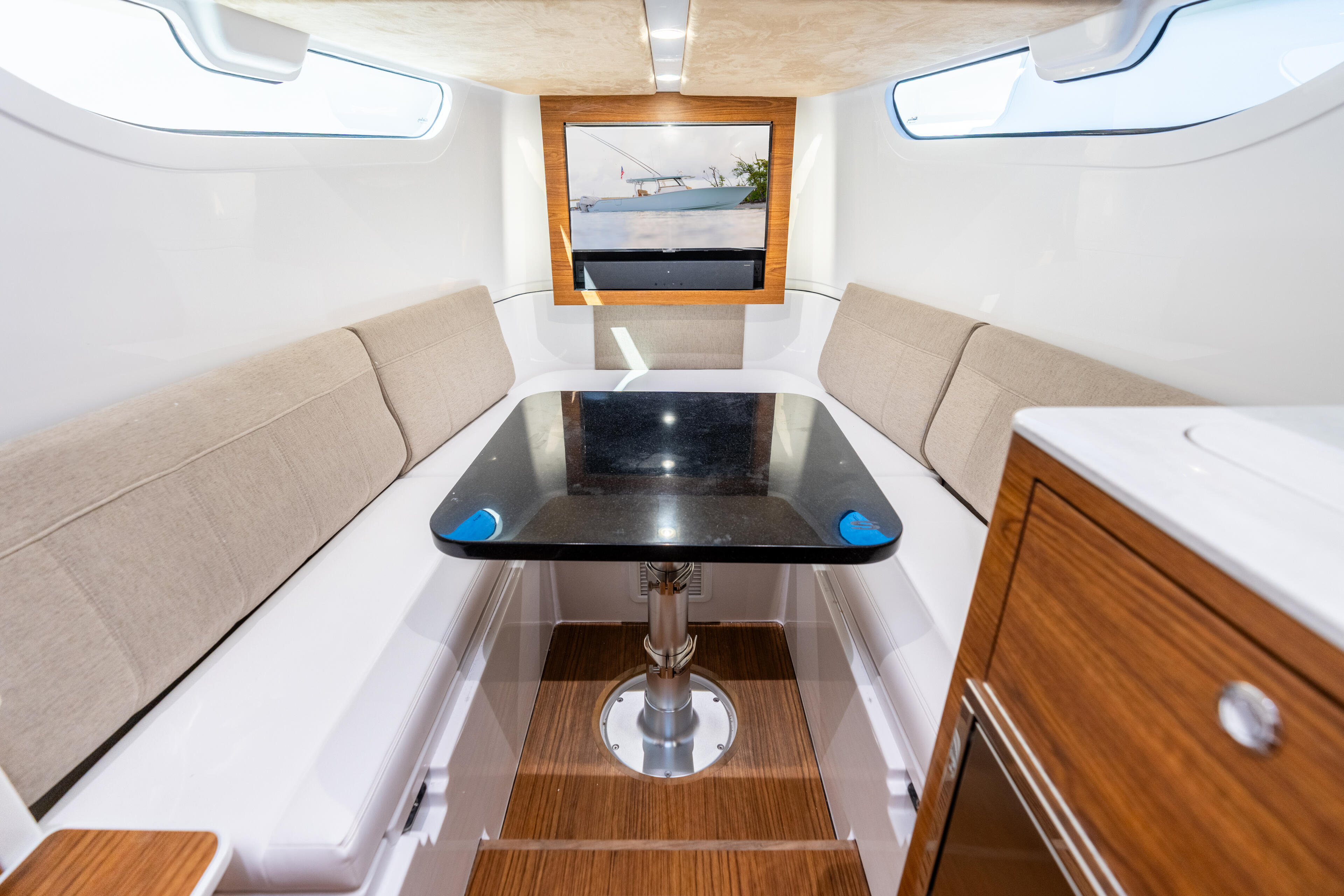 Cabin interior with beige L-shaped seating, black table, wood cabinetry, and skylight windows overlooking water