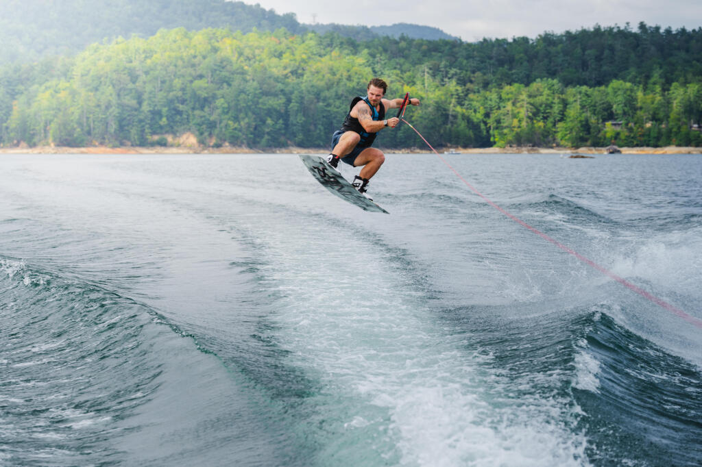 Man wakeboarding behind a boat on a lake with forested shoreline in background