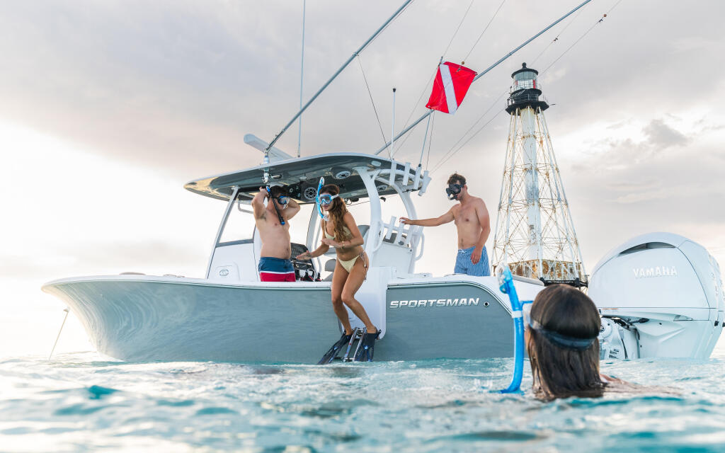 Family and friends swimming and entertaining alongside a Sportsman center console boat anchored in shallow turquoise water