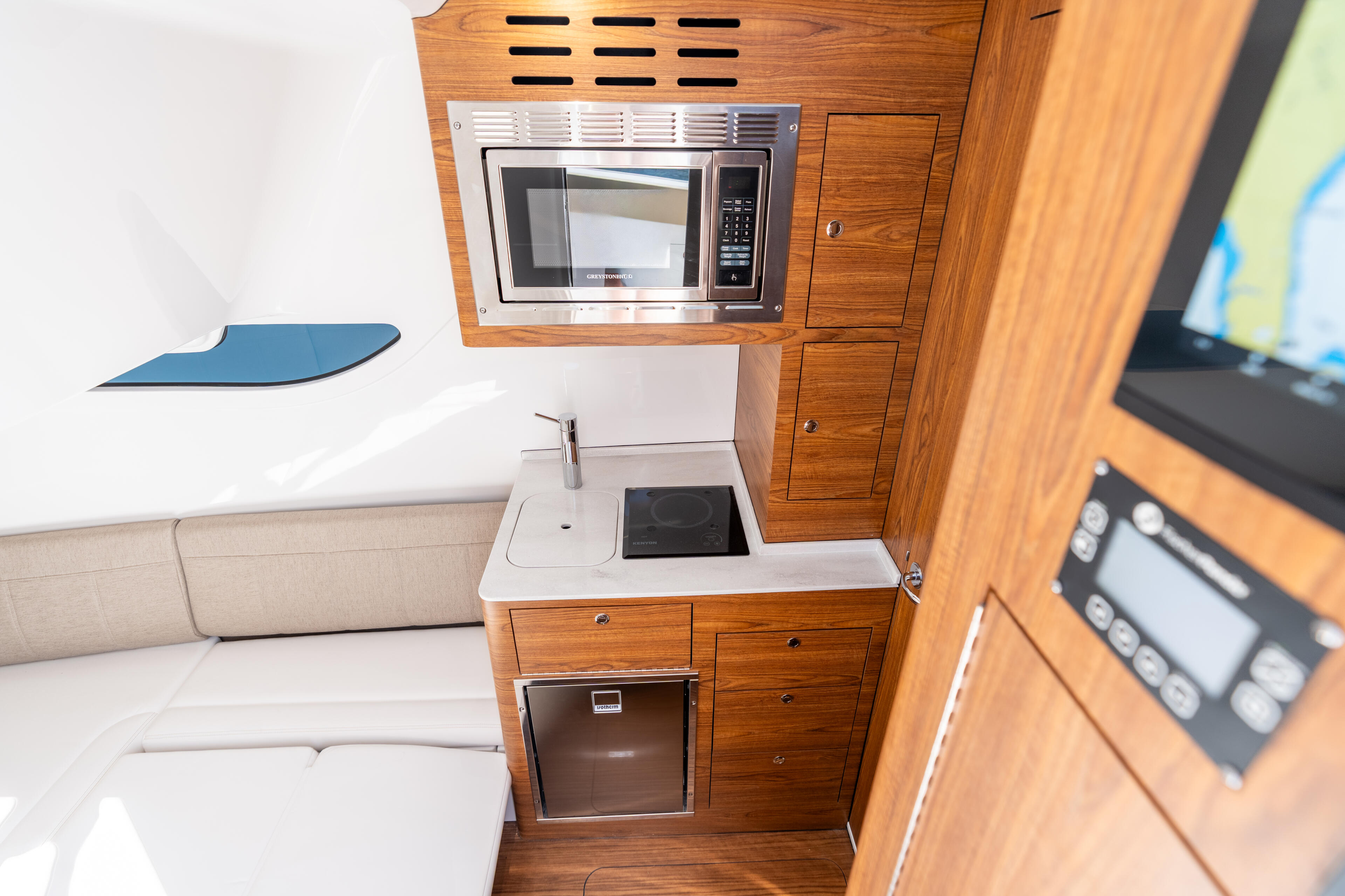 Galley kitchen with wood cabinetry, microwave, cooktop, and storage in boat cabin