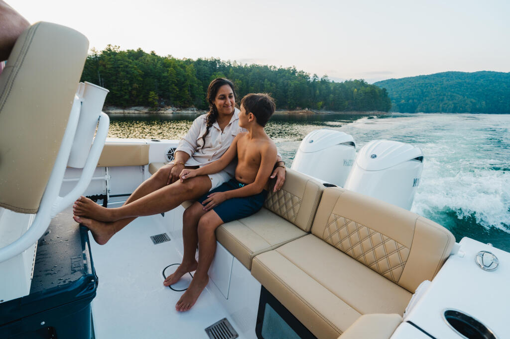 Woman and young boy relax on cushioned seating aboard a boat on a forested lake