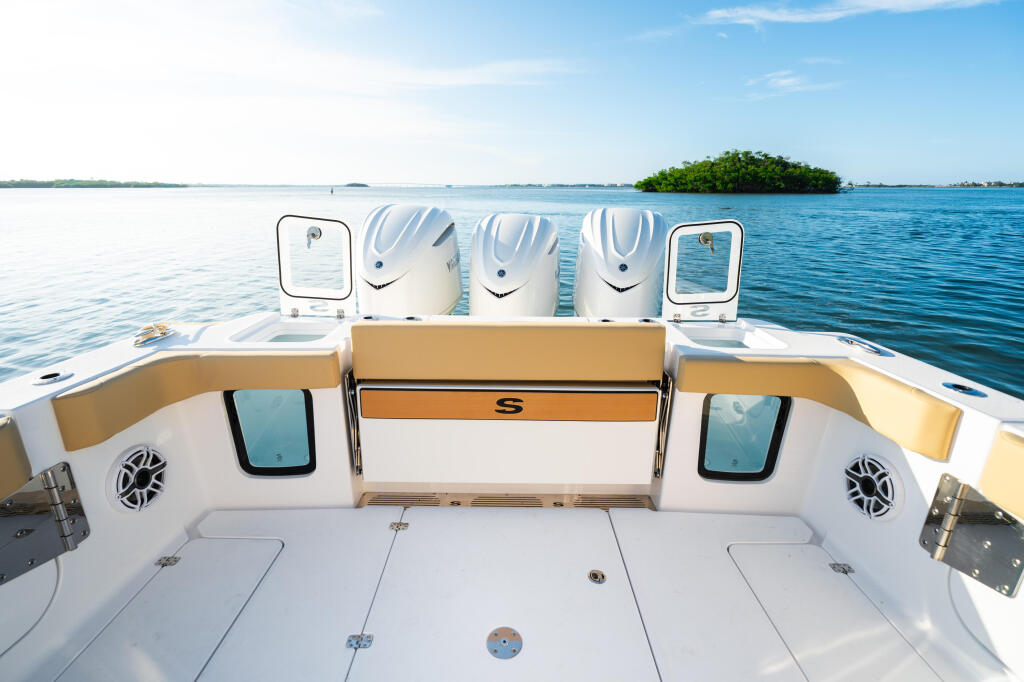 Stern deck of a center console boat with three outboard engines, cushioned seating, and tropical islands visible in calm blue water