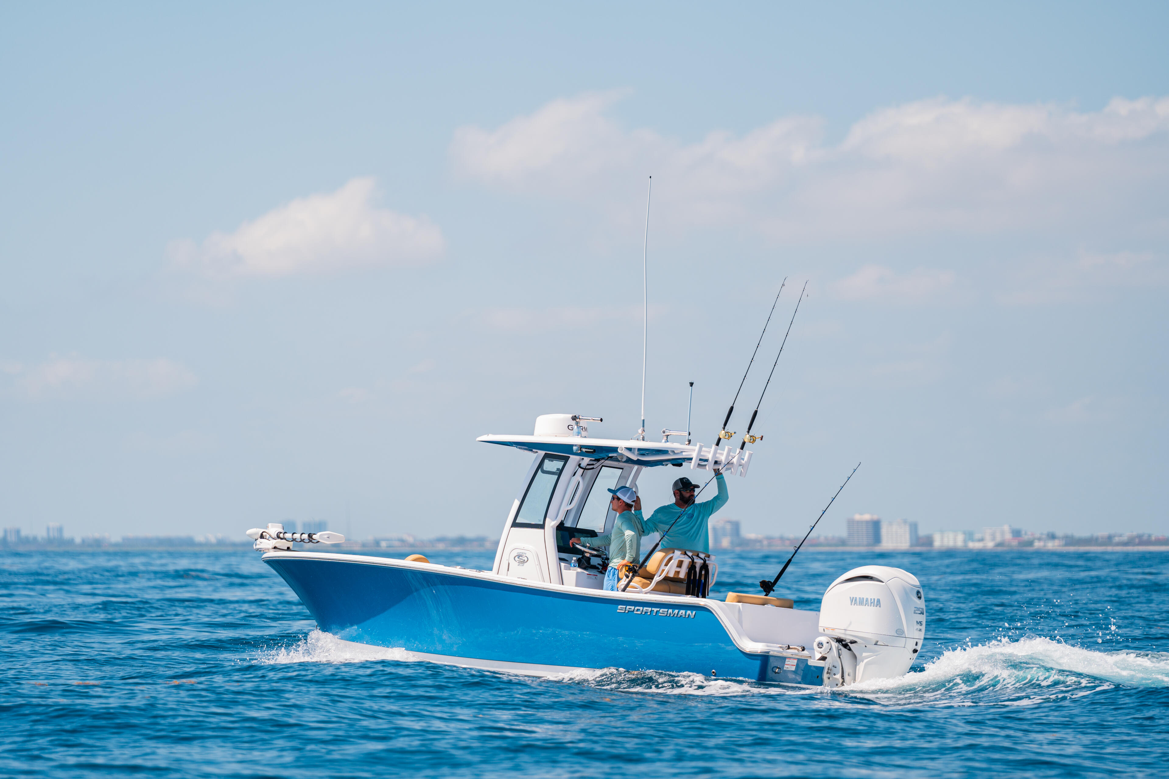 Blue and white sportsman fishing boat running offshore with multiple fishing rods and a hard-top canopy