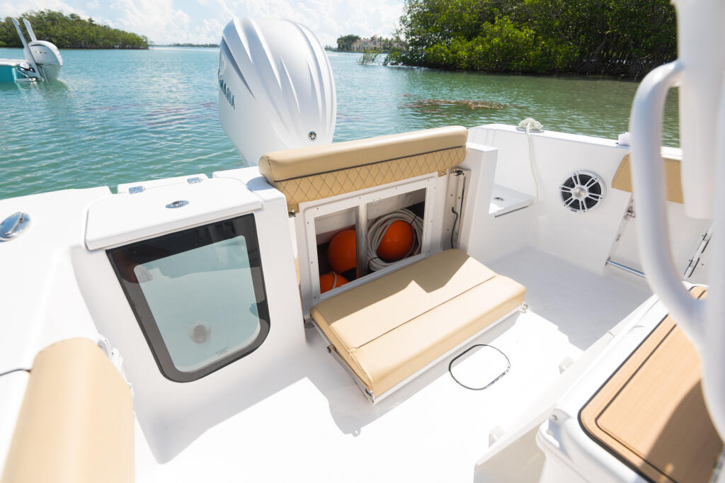 Center console boat showing open rear hatch with storage access and tan cushioned seating near mangrove-lined tropical waters