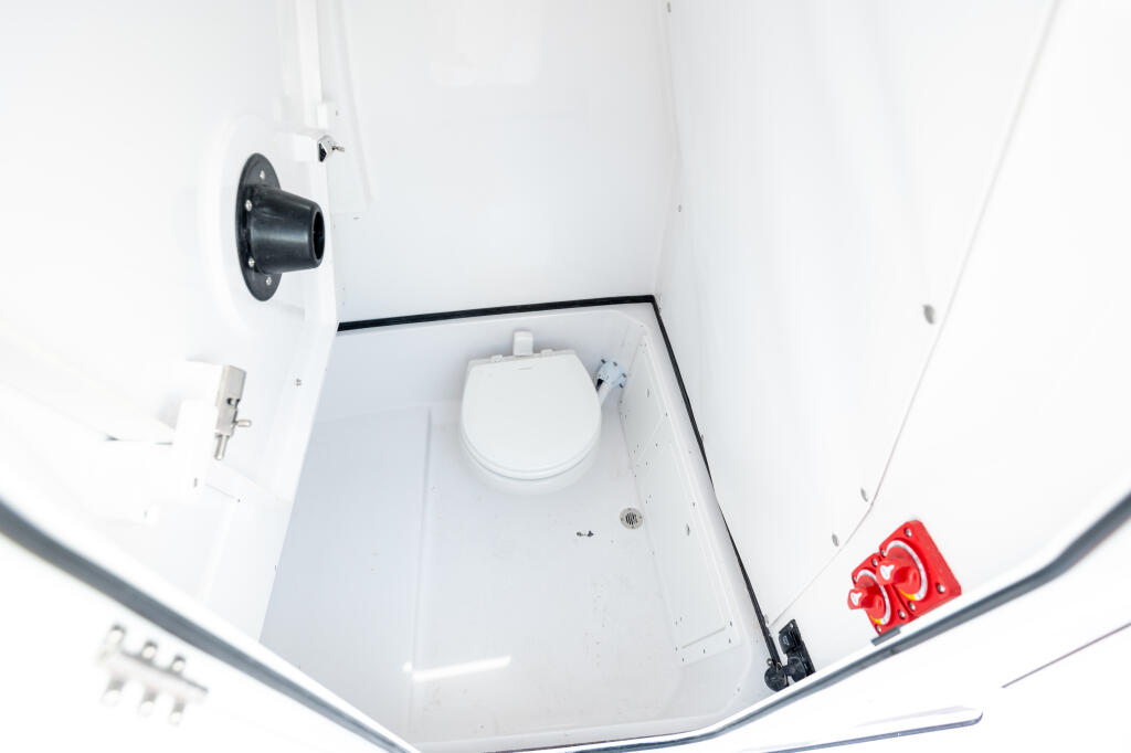 Compact cabin head with white toilet, overhead ventilation, and red lifejacket storage in an enclosed center console boat
