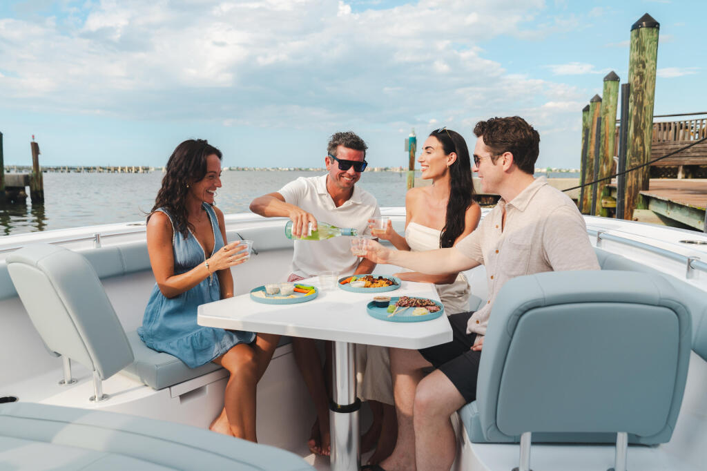 Four friends enjoying drinks and appetizers at a table aboard a boat docked at a marina