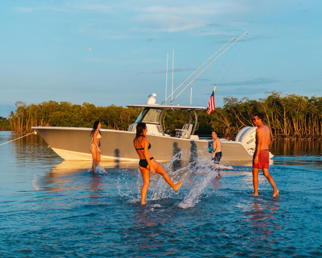 Children splashing and swimming in shallow water near a docked center console fishing boat with mangroves in background