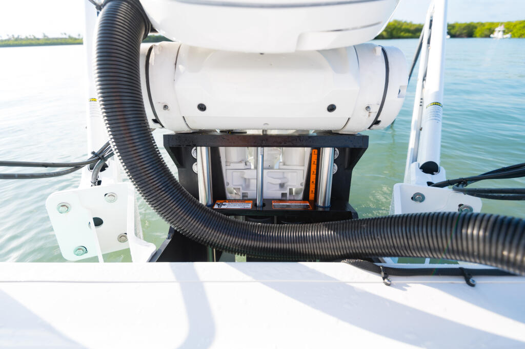 Transom-mounted power jack plate with white cylinder and black corrugated hoses on a boat's stern