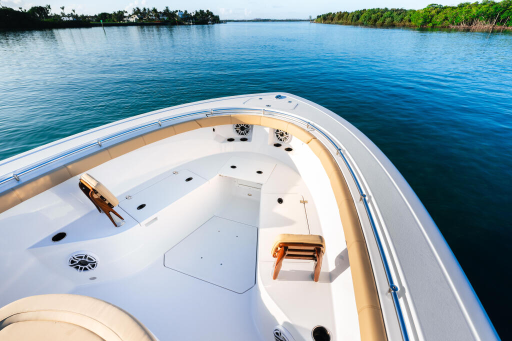 Aerial view of a white center console boat's open bow deck with tan seating and cleats overlooking calm blue water lined with mangroves