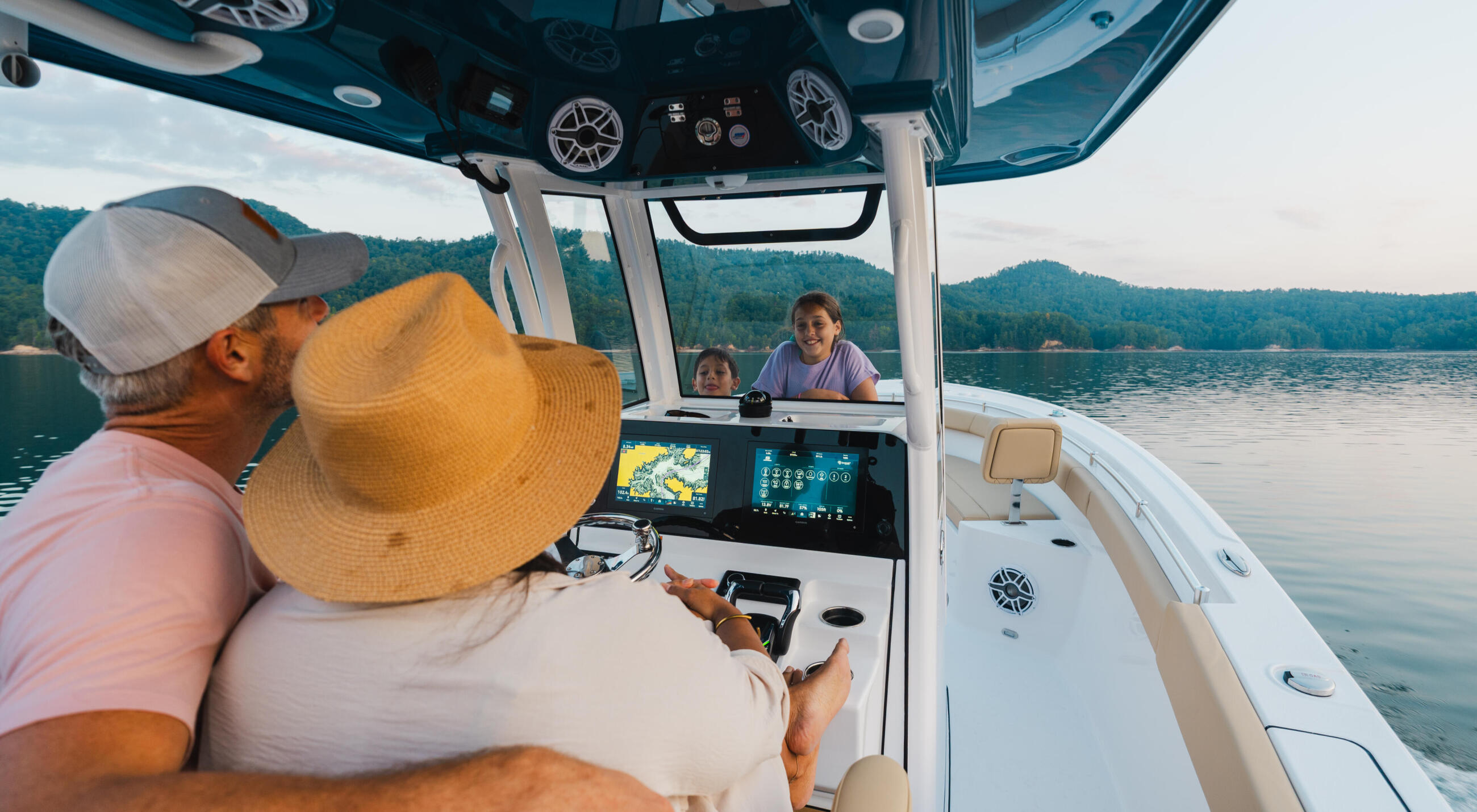 Captain at the helm navigating a center console boat with family members aboard on a scenic mountain lake
