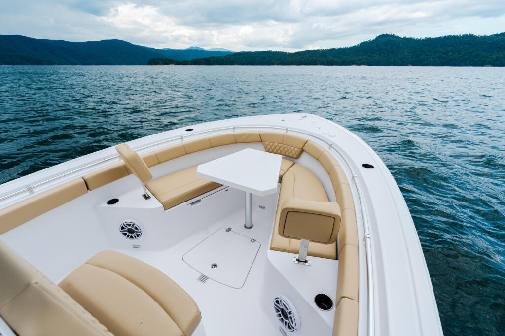 Boat's bow seating area with tan cushioned seats, white deck, and mountain-lined lake in background