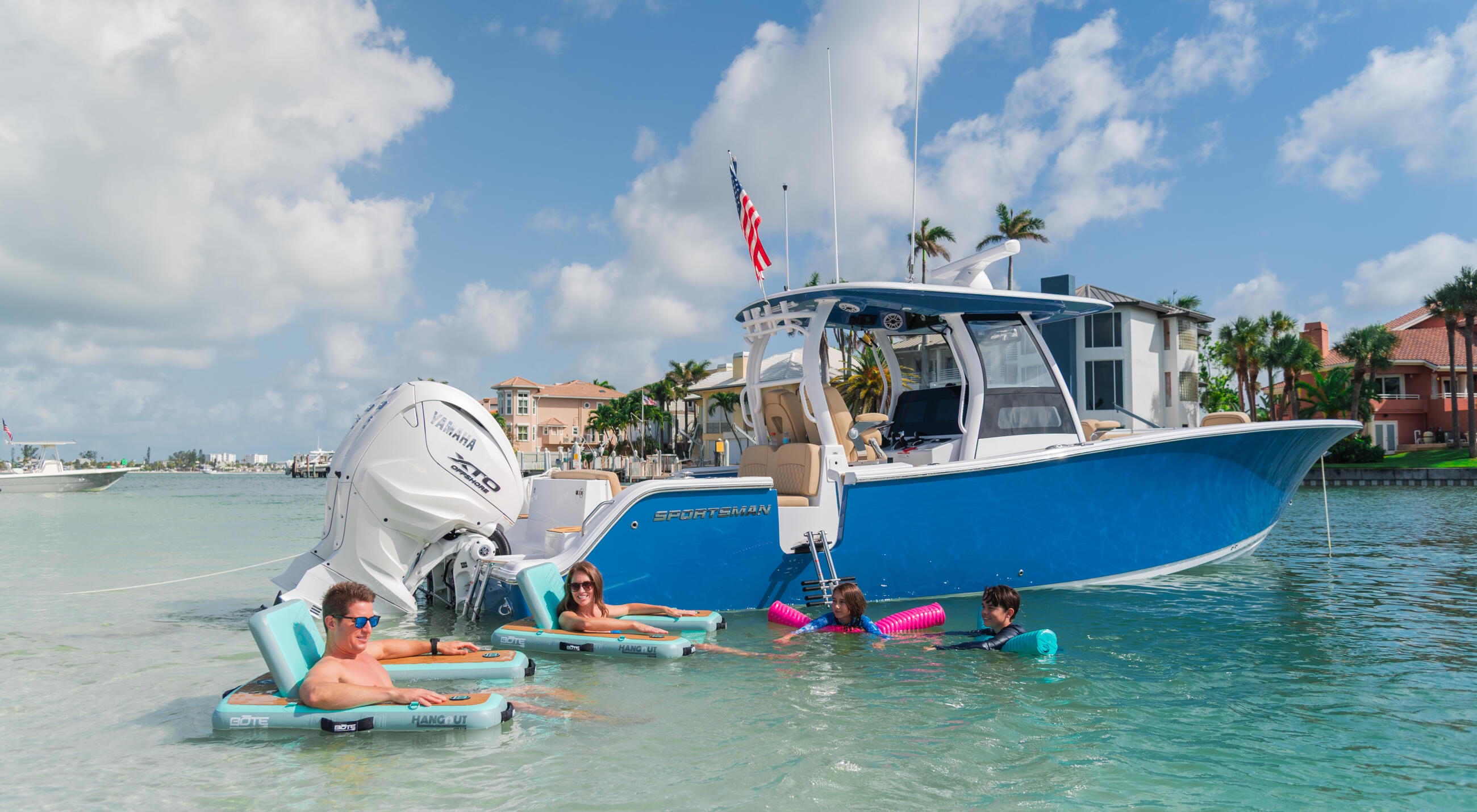 Family swimming and relaxing at a sandbar next to a blue and white center console boat