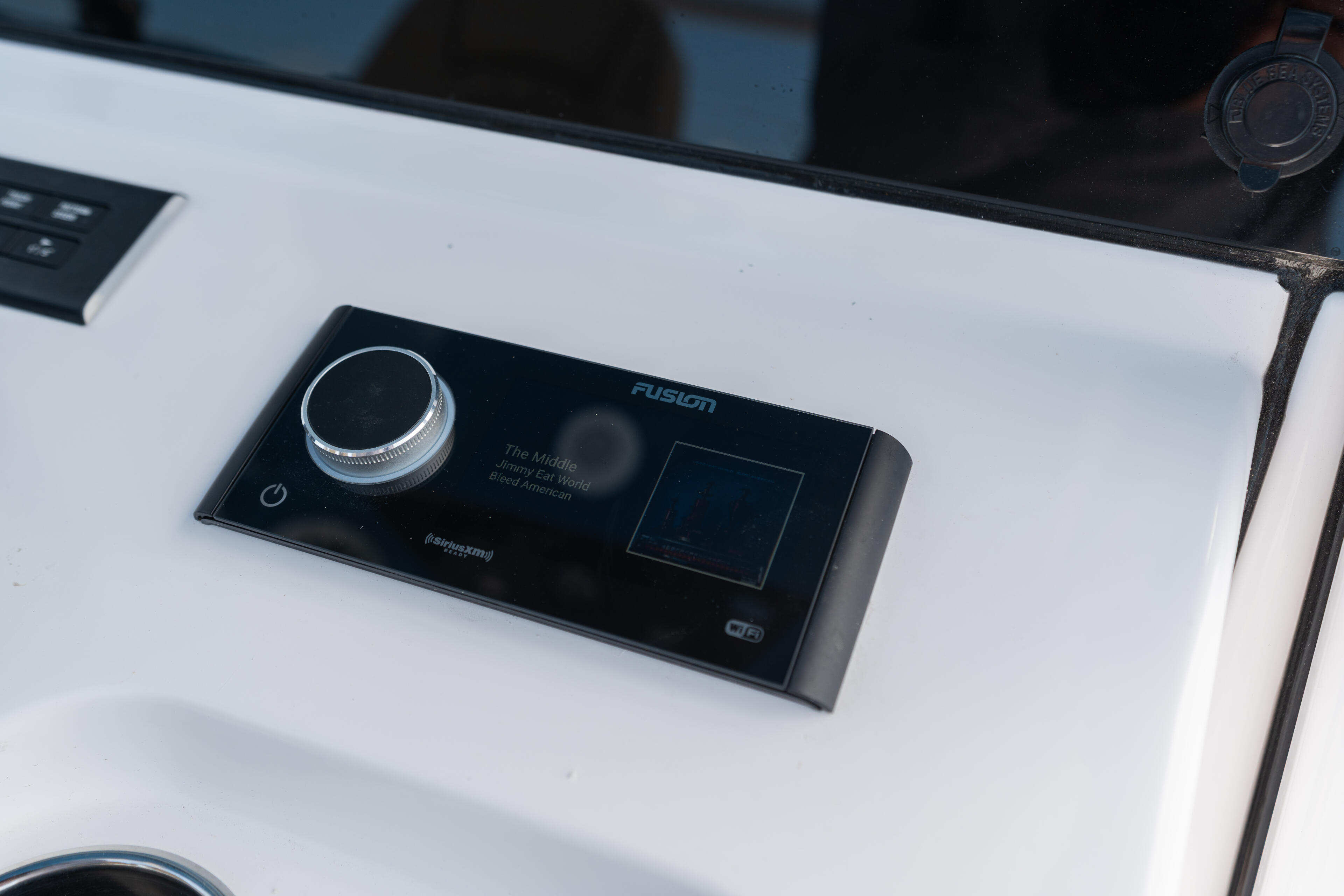 Fusion audio control panel mounted on white boat dashboard with rotary knob and digital display