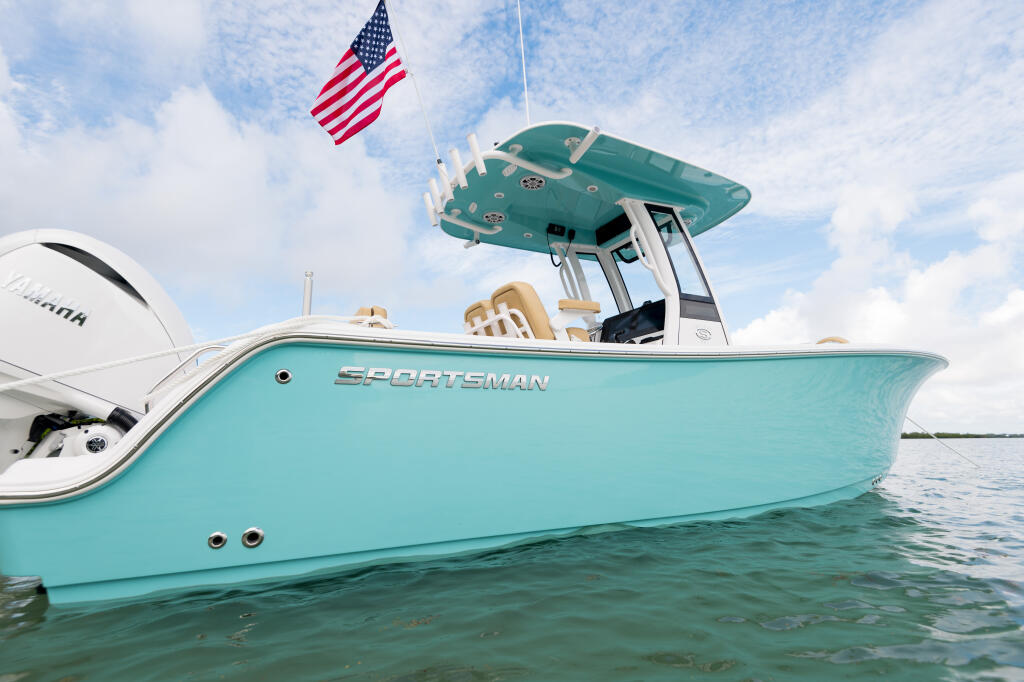 Turquoise Sportsman center console boat with hard-top, engines, and American flag floating in shallow water