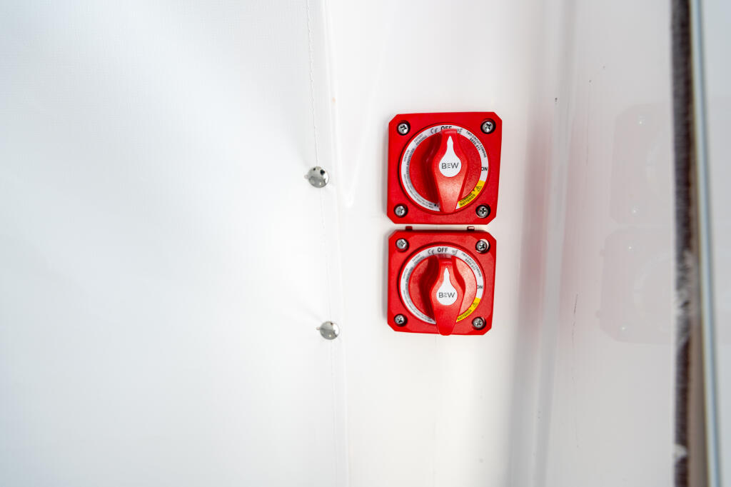 Two stacked red B&W battery disconnect switches mounted on white cabin wall
