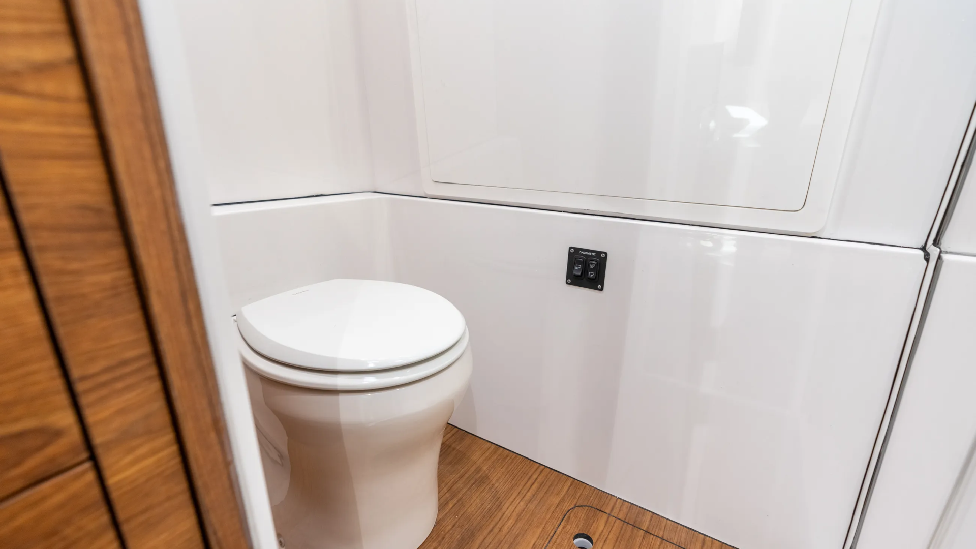 Modern boat cabin head with white porcelain toilet, white fiberglass walls, and wood-grain flooring