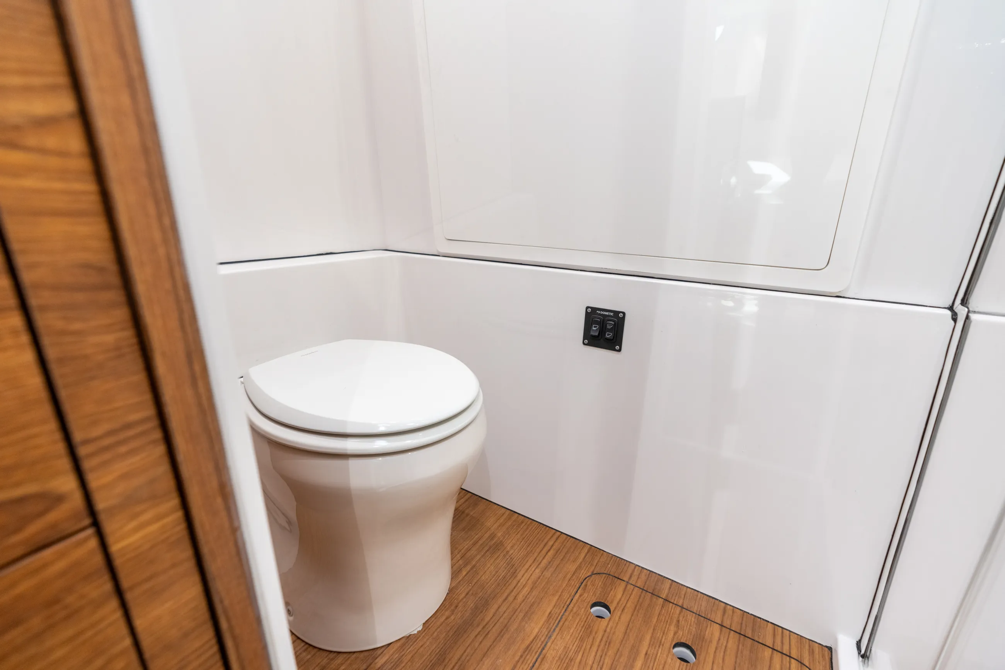 Modern boat cabin head with white porcelain toilet, white fiberglass walls, and wood-grain flooring