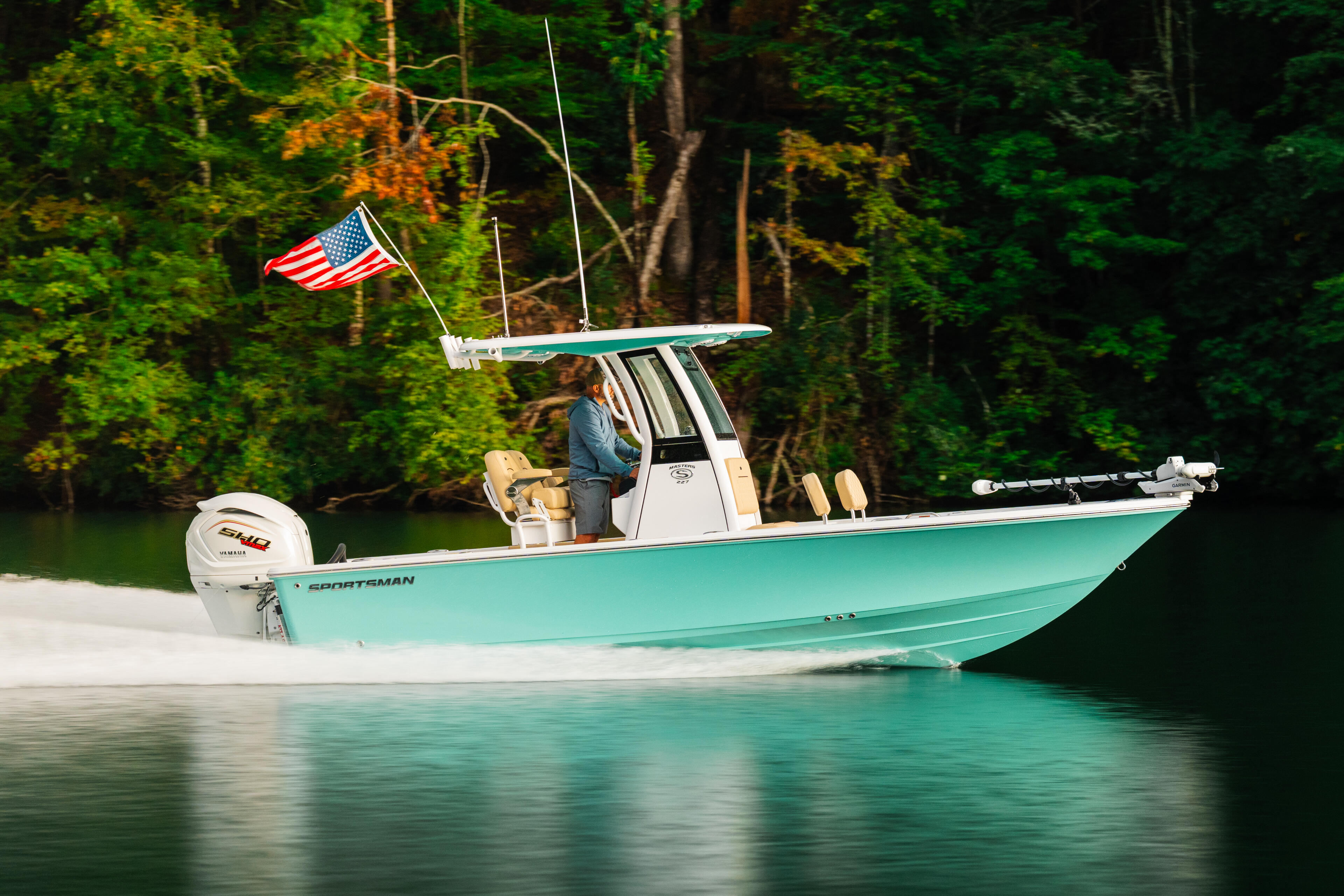 Turquoise fishing boat with American flag moored in clear water against forested shoreline