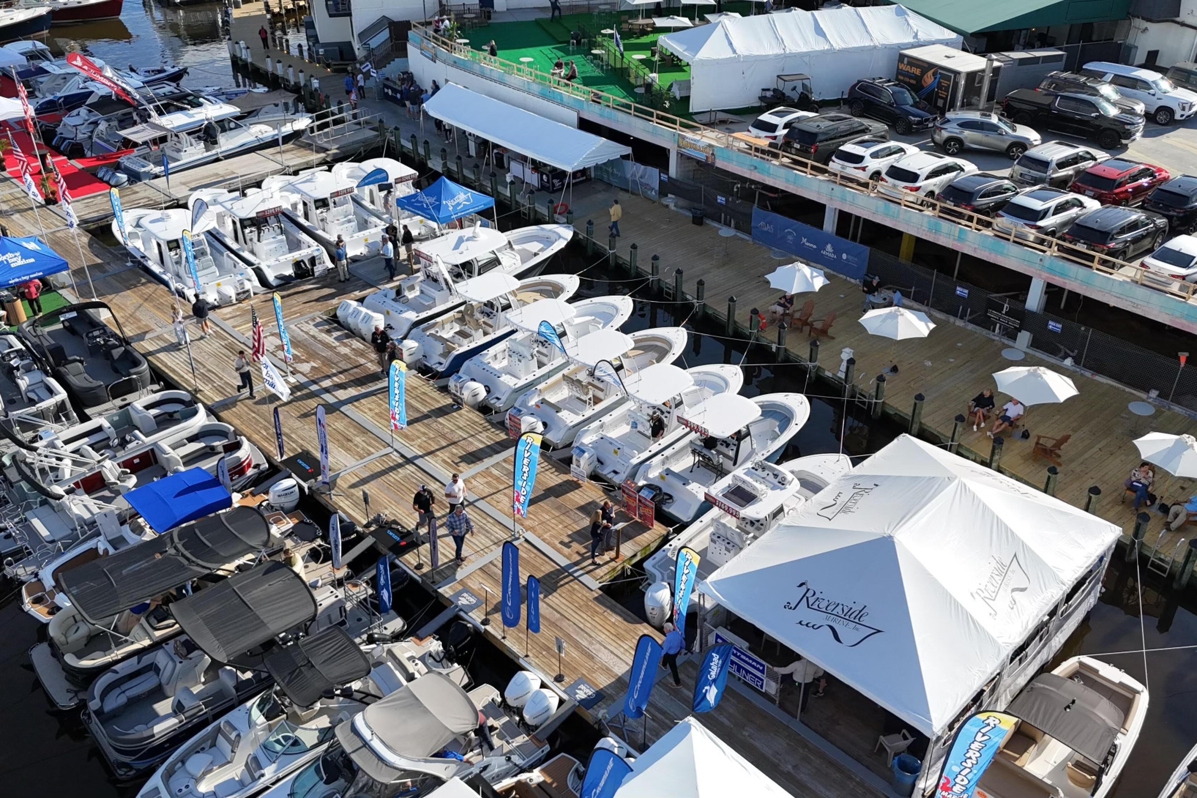 Aerial view of a boat dealership marina with multiple white fishing boats lined up at docks and vehicles parked on the lot
