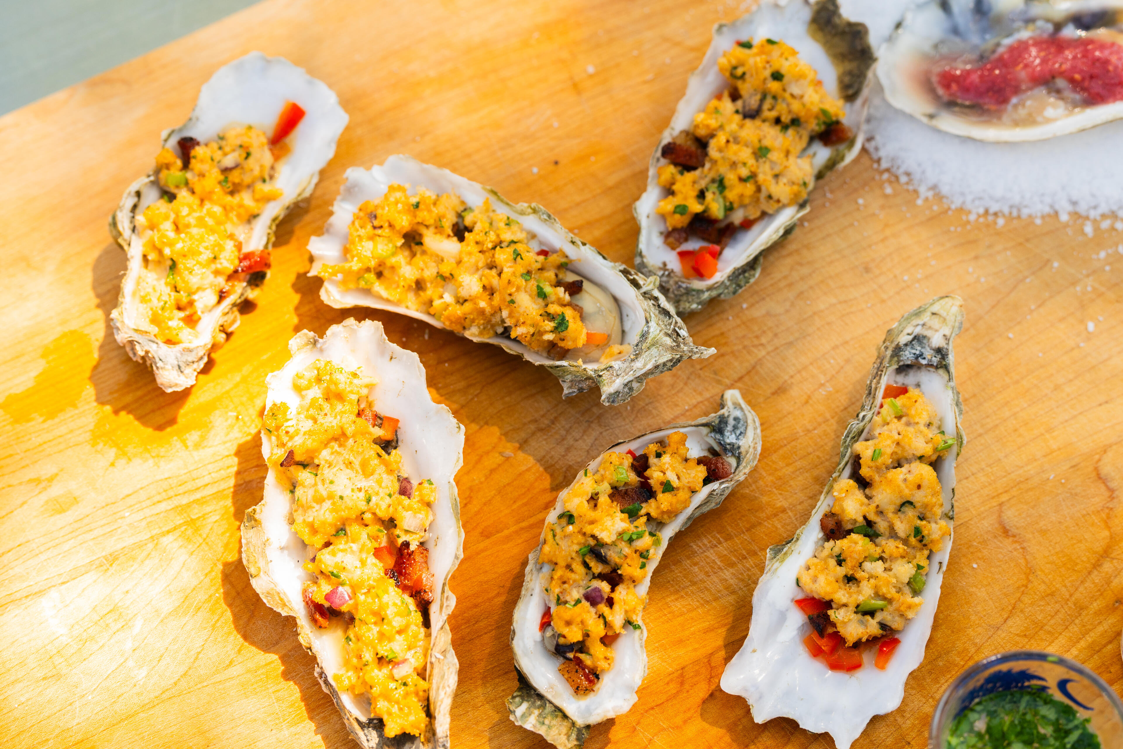 Freshly prepared oysters with golden crumb topping and red peppers on a wooden serving board