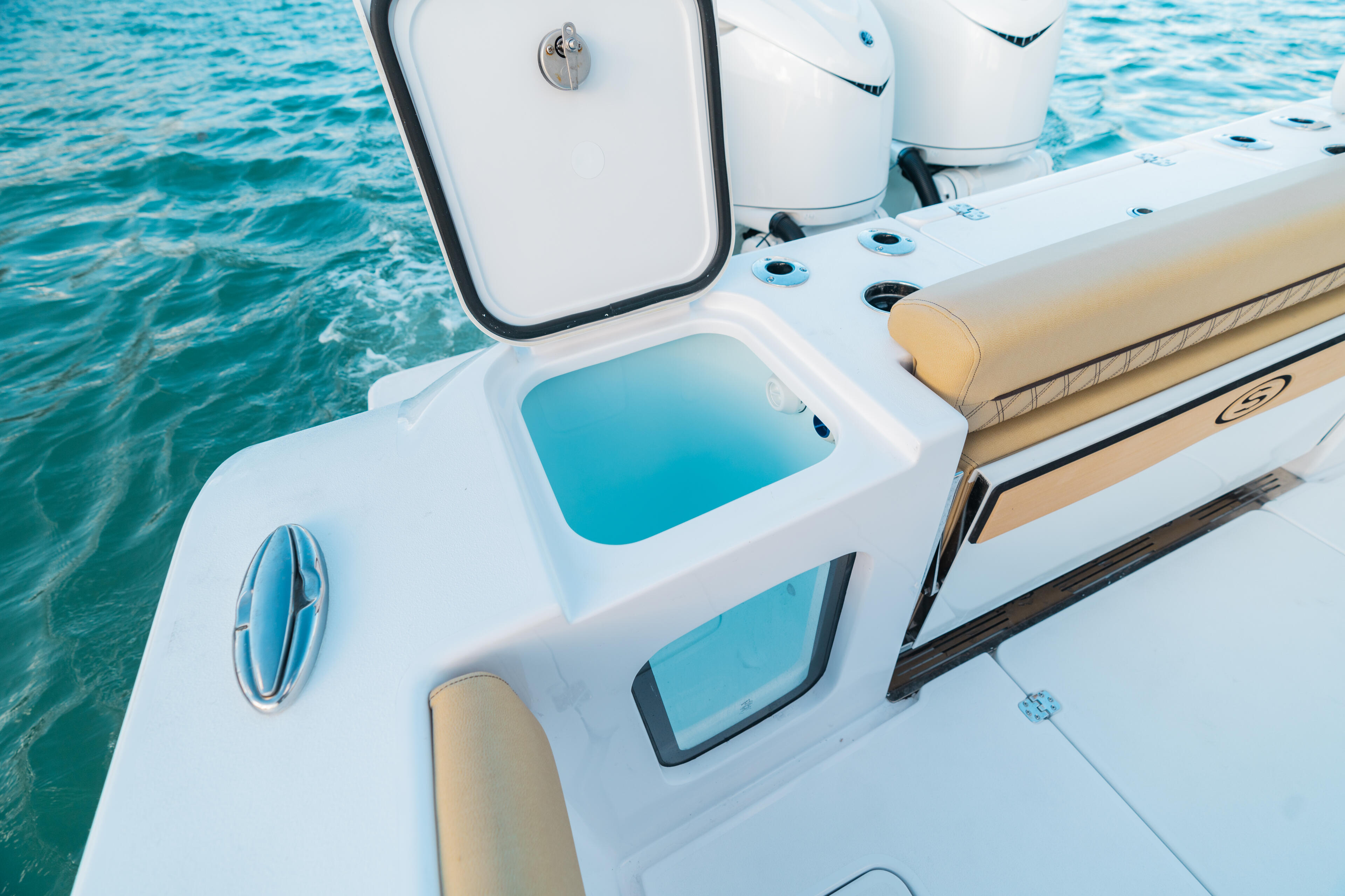 Open center console boat showing livewell, helm seating, and twin outboard engines on turquoise water