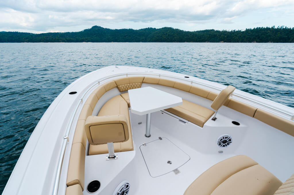 Spacious boat deck with tan seating, white cabin, and forested shoreline across calm waters