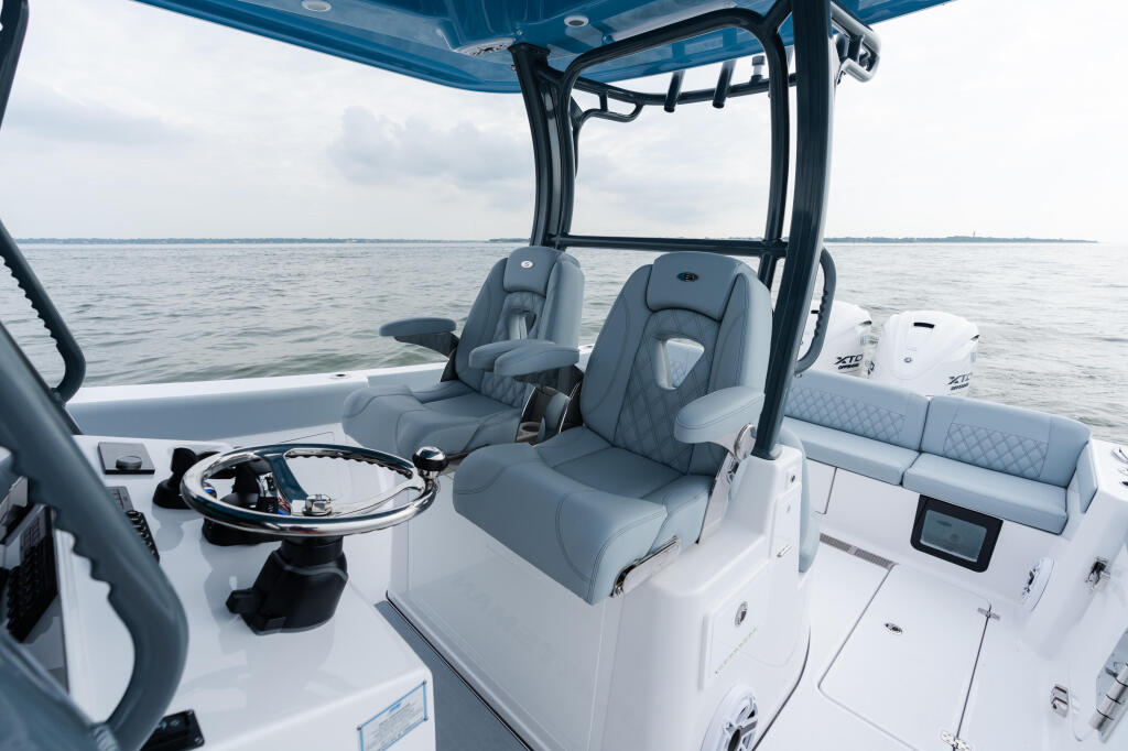 Helm and seating area of a white center console boat with gray cushioned captain's chairs and hard-top canopy on calm ocean water