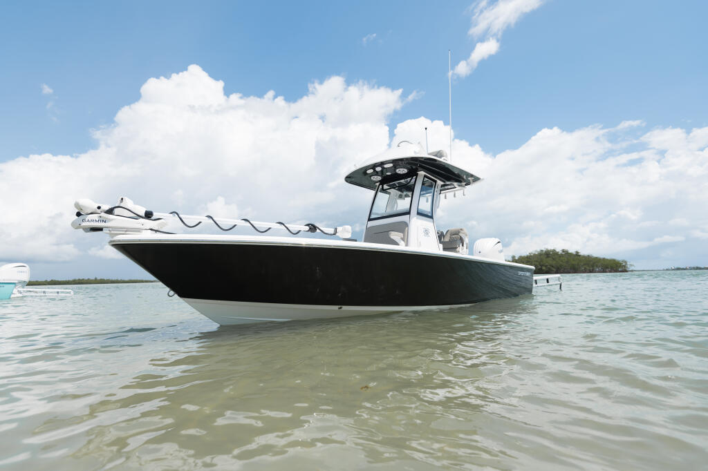 Black and white center console boat with hard-top anchored in shallow tropical waters under blue sky