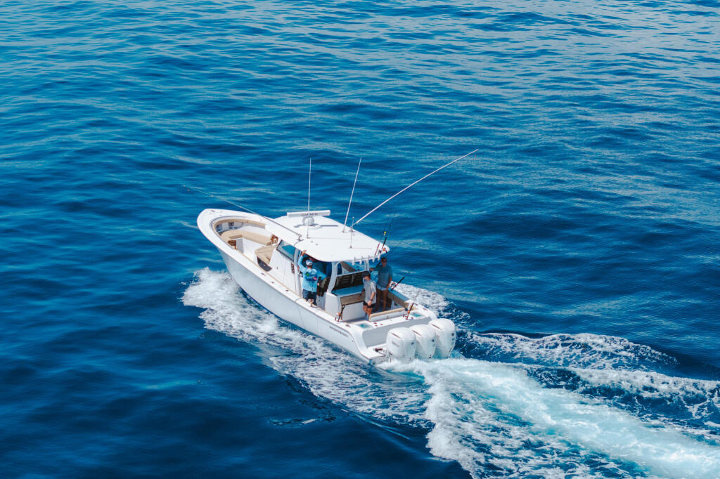 White sport fishing boat running through offshore waters with fishing rods extended