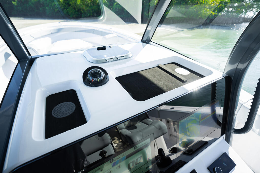 Helm station with compass, controls, and forward windshield view of shallow turquoise water and mangroves