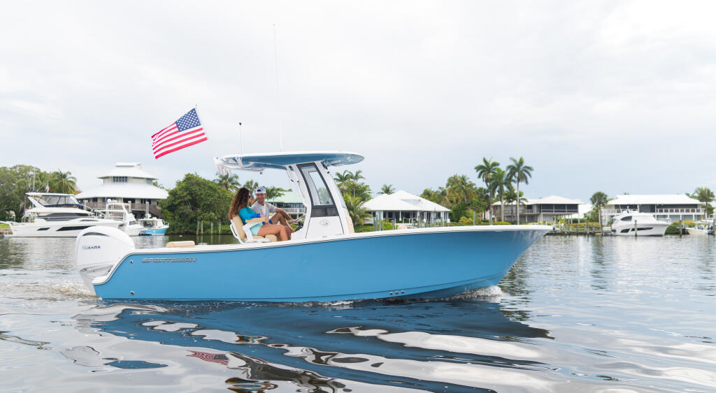 Couple enjoying a blue center console boat anchored at a shallow sandbar with waterfront homes and palm trees in the background