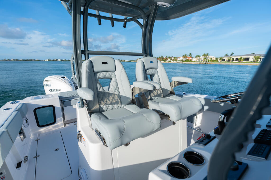 White center console boat with gray quilted seating, hard-top canopy, and waterfront homes visible across the blue water