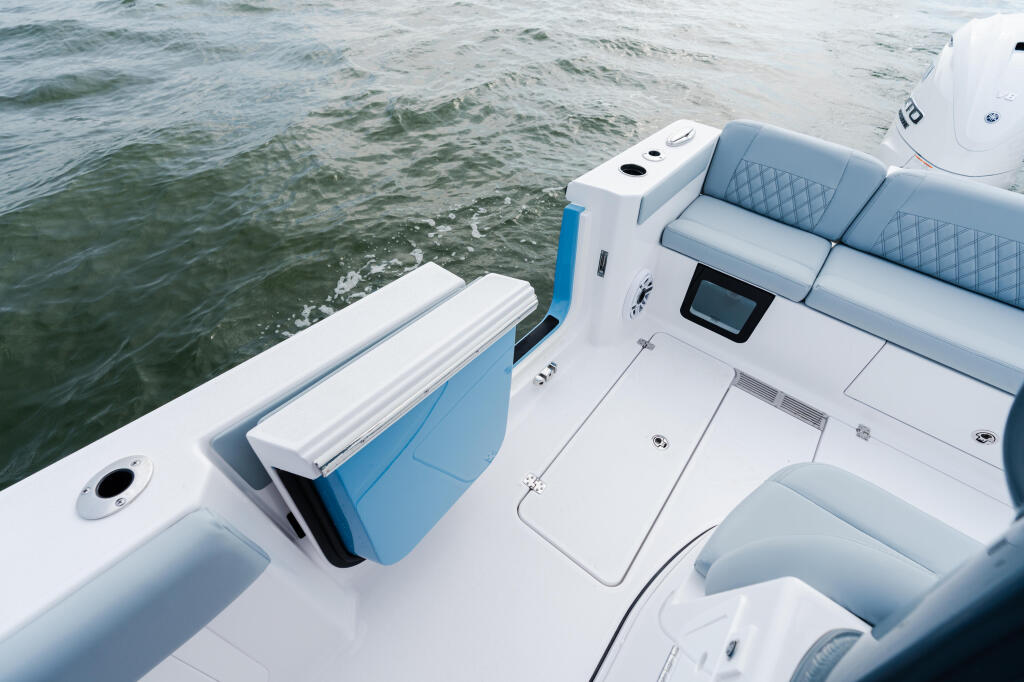 Starboard side seating and console of a white and blue center console boat with calm water beyond