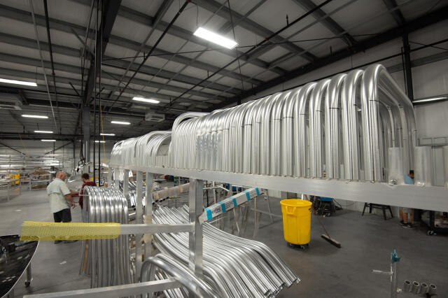 Manufacturing facility with aluminum boat hull sections stacked and organized under industrial lighting