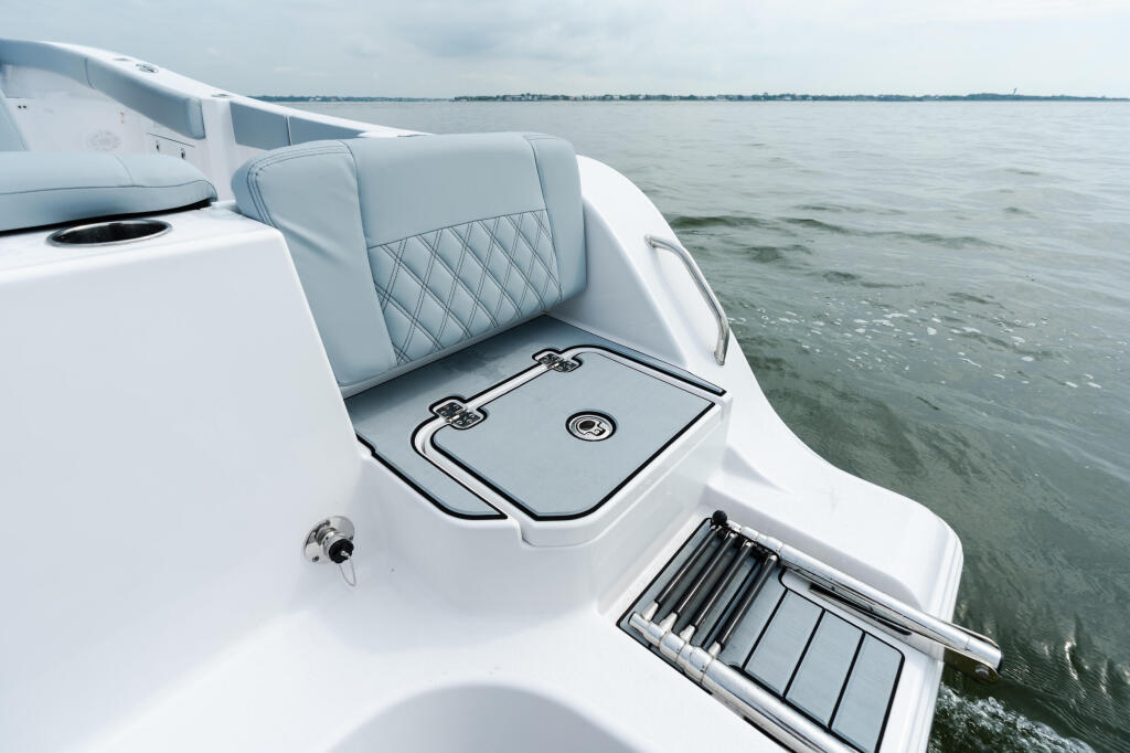 White boat's side console with quilted gray seating, storage locker, and open deck overlooking calm water