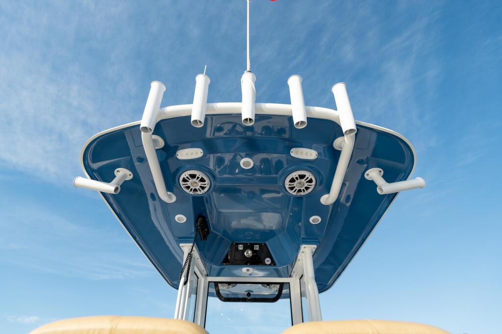 Overhead view of boat's hard-top with white railings, helm station, and lighting fixtures against blue sky