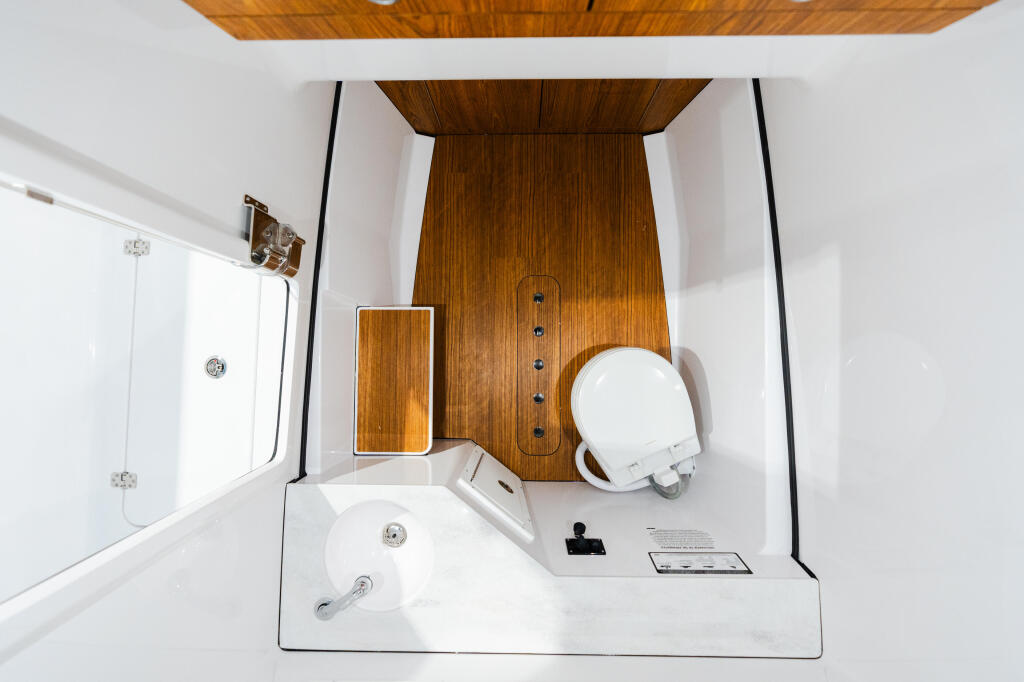 Overhead view of a boat cabin head with white fixtures, wooden ceiling accent, and glass shower enclosure