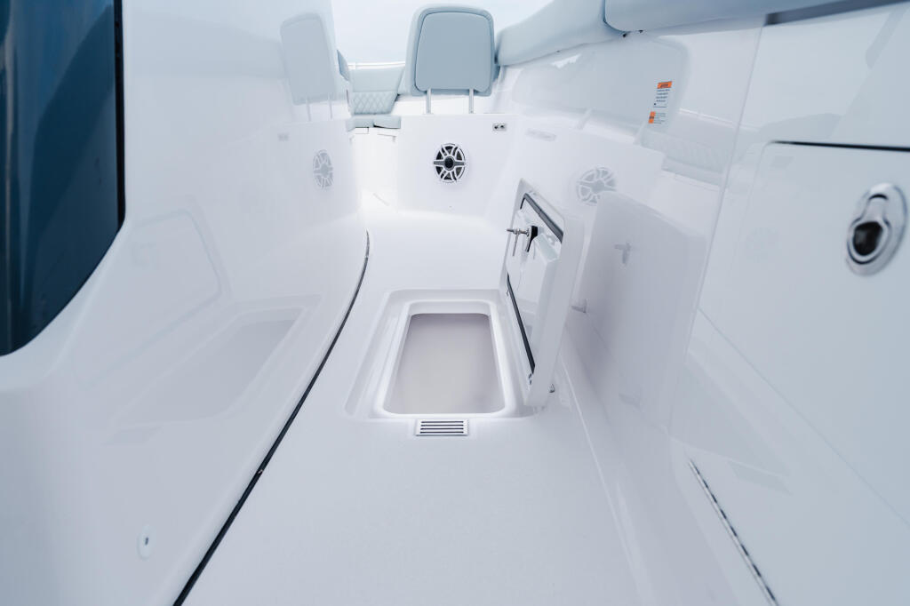 Overhead view of bright white boat cabin with two forward-facing seats, centered hatch, and speaker grilles
