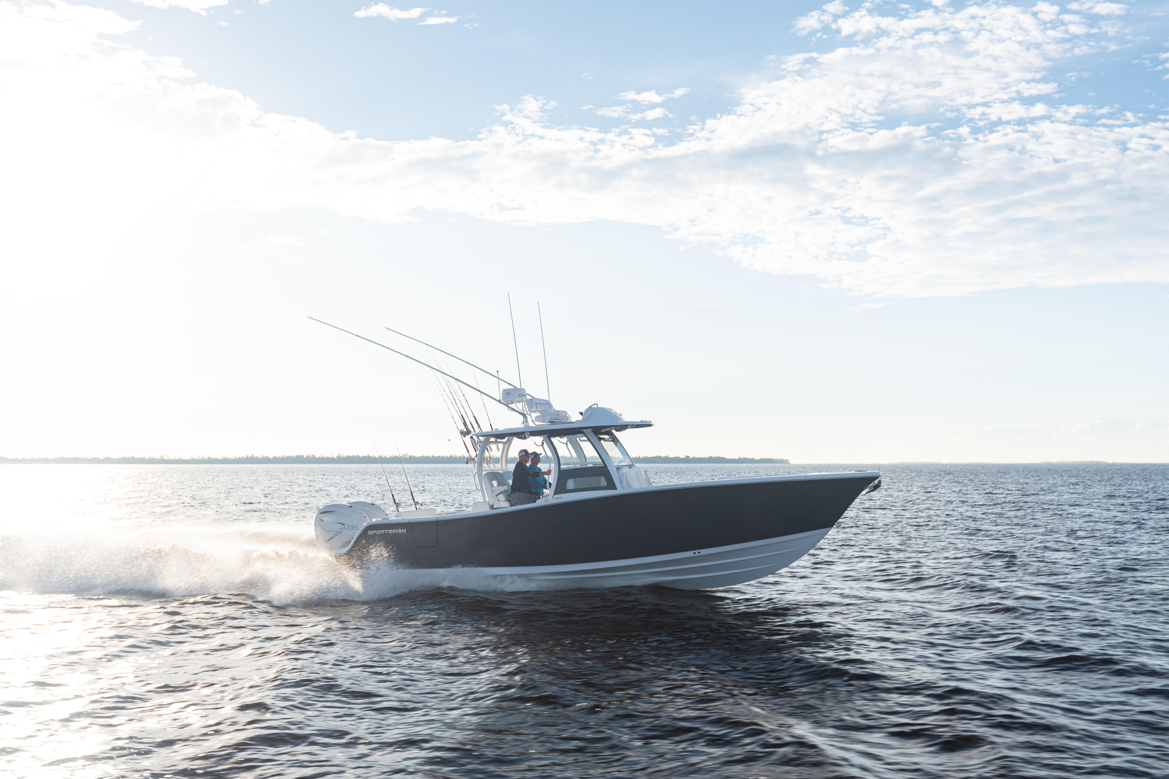 Black and white fishing boat with tall outriggers running through shallow coastal waters