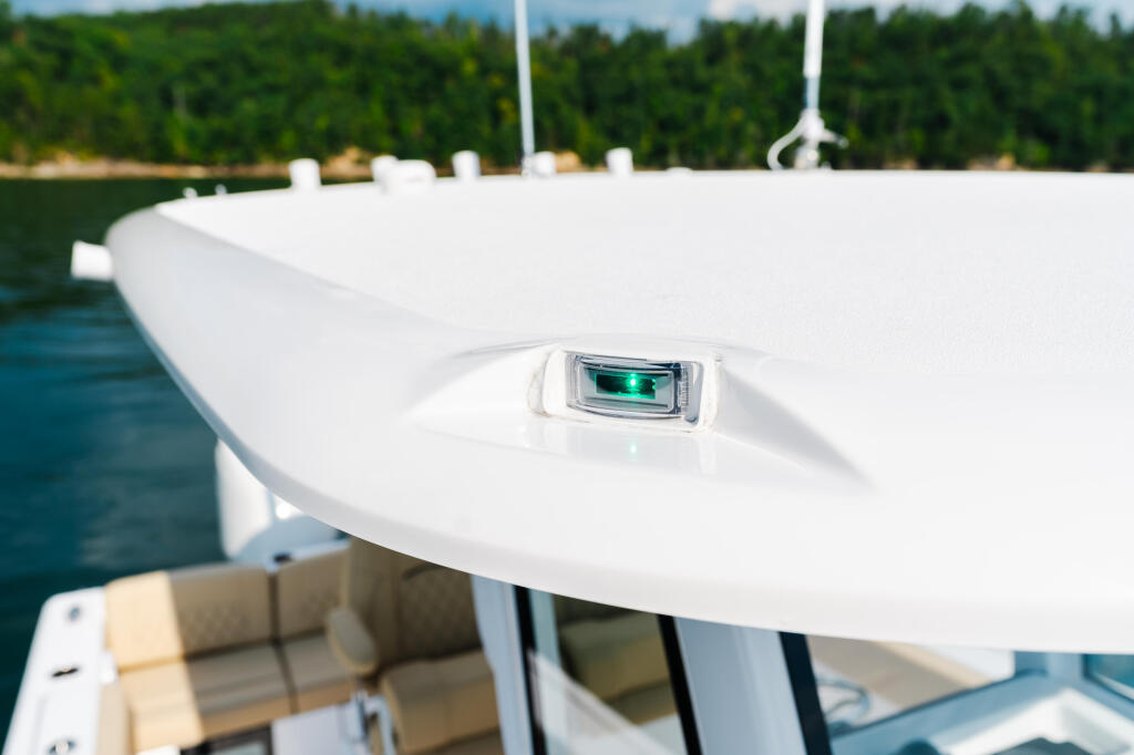 Green navigation light mounted on white fiberglass boat canopy with forest shoreline in background